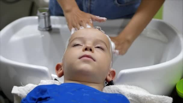 Parekhmacher, po ostříhání dítěte předškolního věku, umýt si vlasy, mýdlo s šamponem, dítě leží odpočívá a užívá si, zatímco oni si myjí vlasy poté, co mají jejich účes střih.Dětský účes — Stock video