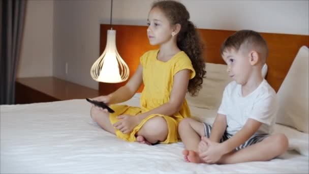 Retrato de niños pequeños y lindos viendo la televisión en casa por la noche mientras están sentados en una cama grande solos. Niño y niña viendo dibujos animados divertido y triste, amable y aterrador en el cine en casa en la vida — Vídeo de stock