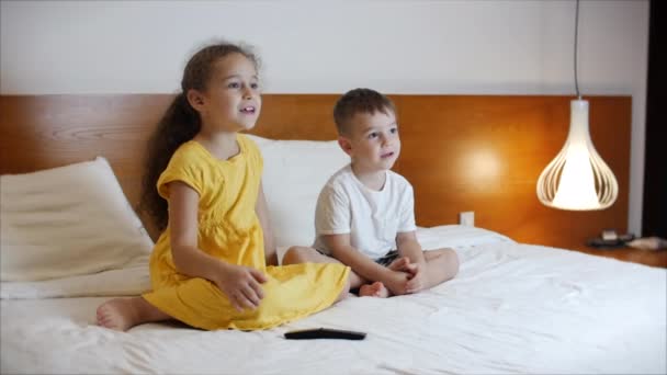 Portrét roztomilých malých dětí, které se večer doma dívají na televizi, zatímco sedí samy na velké posteli. Chlapec a dívka sledující karikatury zábavné a smutné, laskavé a děsivé v domácím kině v životě — Stock video