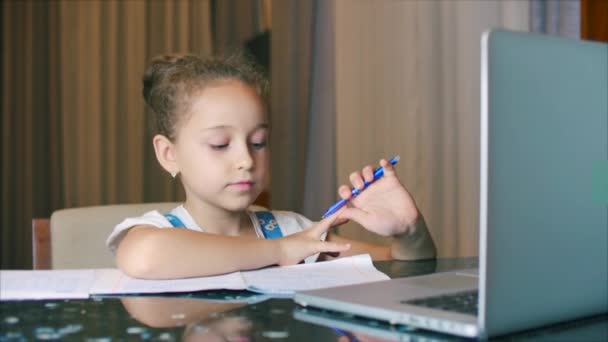 Liten flicka en söt grundskola barn 7-8 år gammal hemma studerar i familjelärande lyssnar på skolföreläsningar gör läxor utan att lämna hemmet.barn hemundervisning, barn utbildning koncept — Stockvideo