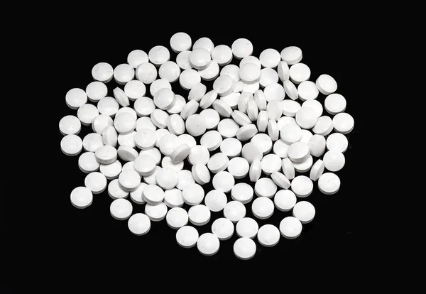 黒い背景に分離した白い錠剤のヒープ — ストック写真