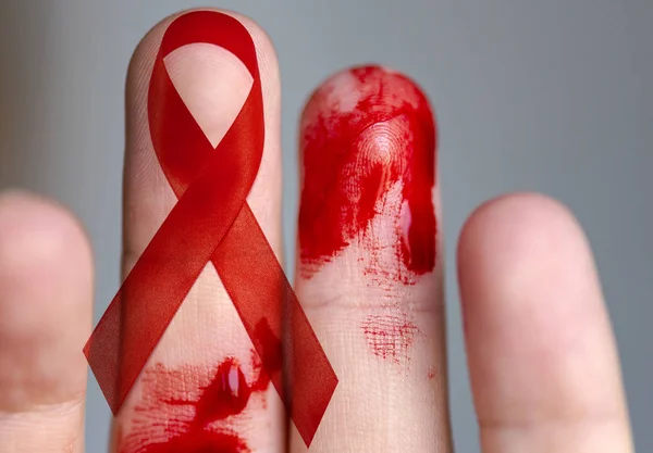 Finger with Blood and Red Ribbon - as Symbol of Supporting and Hope -conceptual Picture about situation with HIV and AIDS in the World