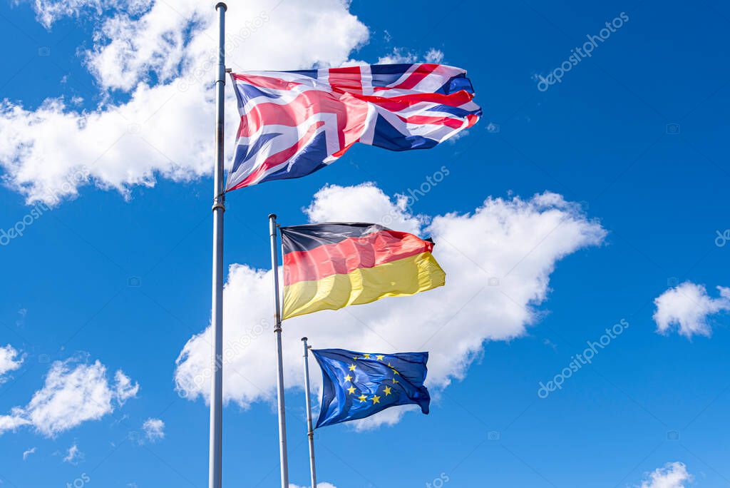 Flags of Germany, Great Britain and European Union in a street. EU, UK and German flags against blue sky