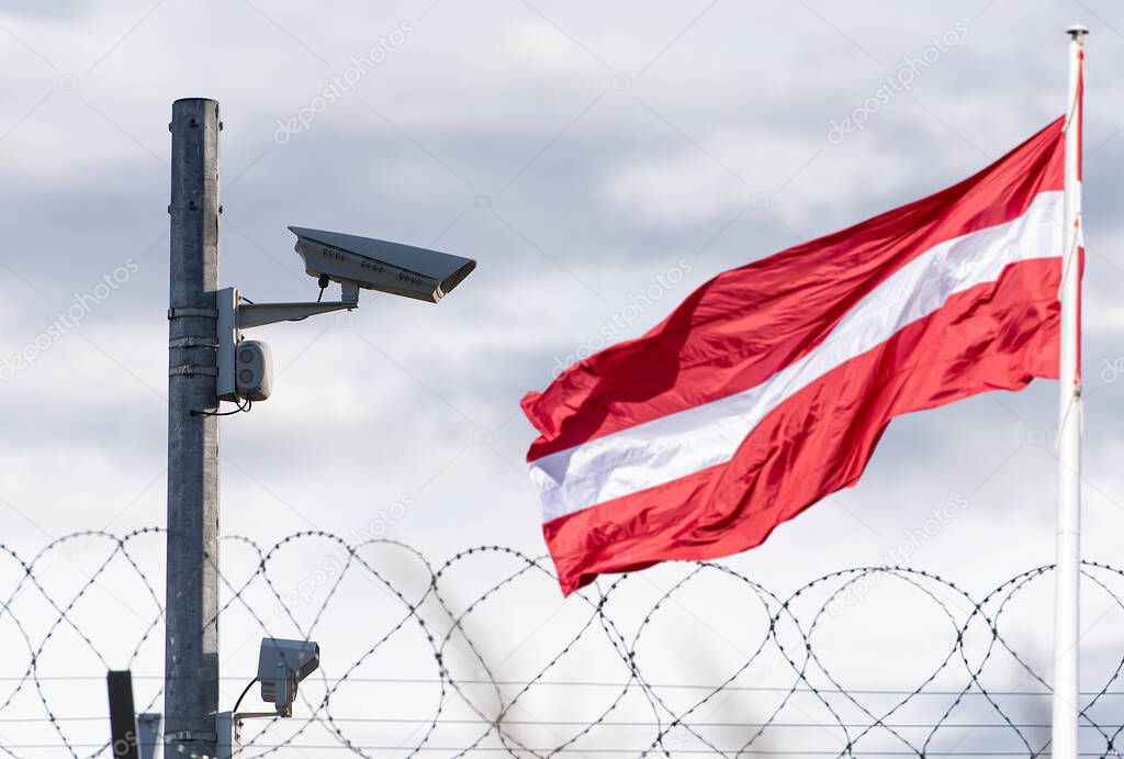 Latvian flag and border with surveillance camera and barbed wire, concept picture