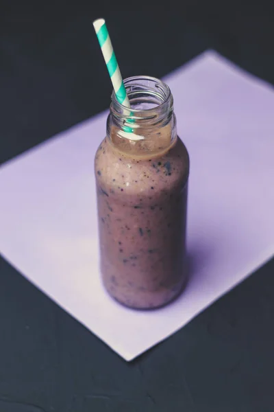 管とガラスの瓶にスムージー 暗い背景と紫の紙の上のブルーベリーとバナナのスムージー — ストック写真
