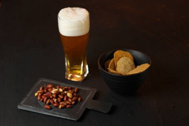 Siyah bir arka plan üzerinde bir cam kasede Light bira. Bira bar ve aperatifler, cips, Kuruyemiş.