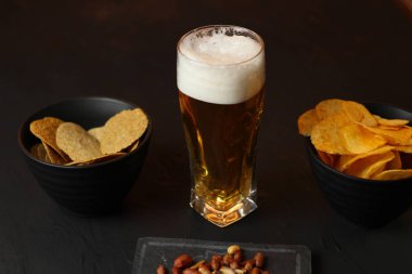 Siyah bir arka plan üzerinde bir cam kasede Light bira. Bira bar ve aperatifler, cips, Kuruyemiş.