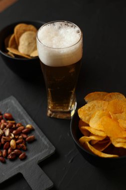 Siyah bir arka plan üzerinde bir cam kasede Light bira. Bira bar ve aperatifler, cips, Kuruyemiş.