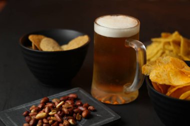 Siyah bir arka plan üzerinde bir cam kasede Light bira. Bira bar ve aperatifler, cips, Kuruyemiş.