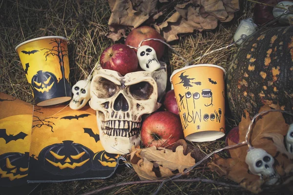 Halloween soon Autumn composition with halloween decorations. Skull,paper glass, garland, pumpkin. Straw backgtound.