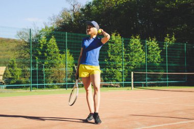 Kısa saç kesimi ile sarışın kız portresi. Arka plan Tenis Kortu. Koyu mavi t-shirt polo ve sarı şort. Çekim spor.