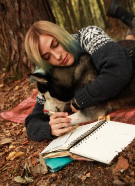 Siberian dış yapraklar bir dinlenme onun metresi ile sonbahar ormanda yaşıyor. Kız bir şapka örme kazak bir kitap okur ve tozluk ile etek. Siyah ve beyaz köpek ve tüylü yaprakları.