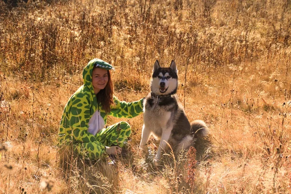 Siberian Husky and red-haired girl in a dragon suit meet the sunrise in the field in the Ukrainian Carpathians. A black and white dog is playing with a woman. Cute Husky.