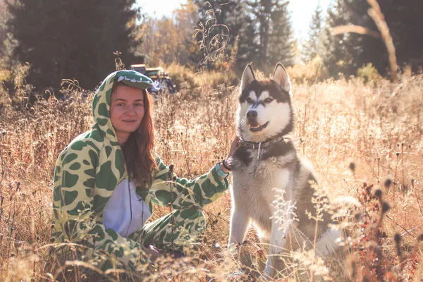 Siberian Husky and red-haired girl in a dragon suit meet the sunrise in the field in the Ukrainian Carpathians. A black and white dog is playing with a woman. Cute Husky.