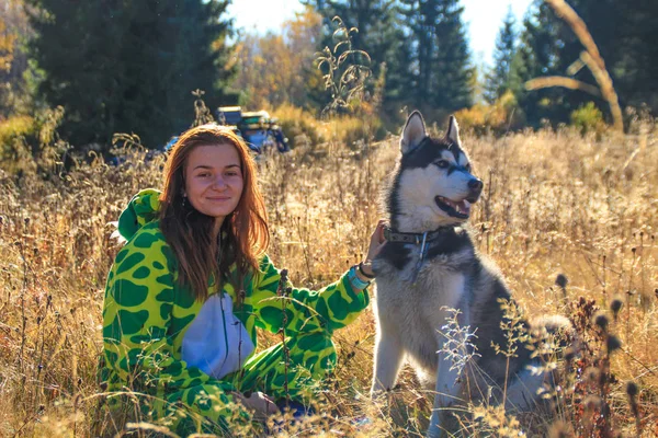 Siberian Husky and red-haired girl in a dragon suit meet the sunrise in the field in the Ukrainian Carpathians. A black and white dog is playing with a woman. Cute Husky.