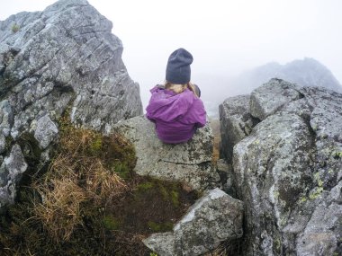 Kız dağ manzaralı bir uçurumun kenarında oturur. Ukraynalı Karpat Dağları. Sisin içinde seyahat.