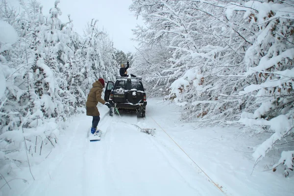 Dziewczyna Idzie Snowboard Przywiązaną Samochodu Człowiek Idzie Sanki Przywiązane Samochodu — Zdjęcie stockowe