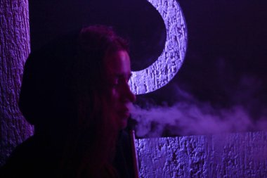 Bir nargile ve nefes duman içinde belgili tanımlık geçmiş mor bir ifade ile sigara içen bir kız portresi. Cafe. Bar. Sanatsal Fotoğraflar