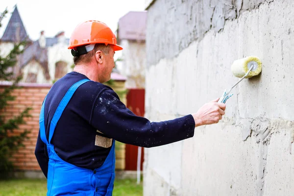 A builder in an orange building mask in his hands with a roller