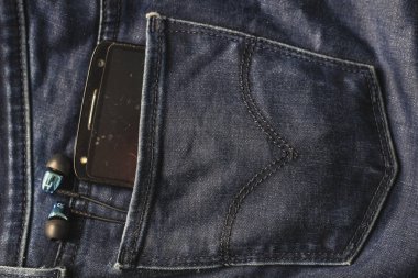 Kulaklıklar ve kotpantolonun arka cebinde siyah bir telefon. Kopya S
