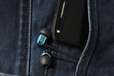 Kulaklıklar ve kotpantolonun arka cebinde siyah bir telefon. Kopya S