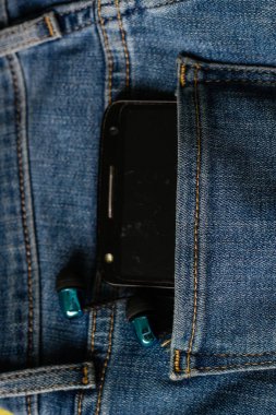Kulaklıklar ve kotpantolonun arka cebinde siyah bir telefon. Kopya S