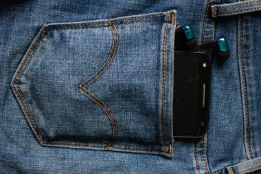 Kulaklıklar ve kotpantolonun arka cebinde siyah bir telefon. Kopya S