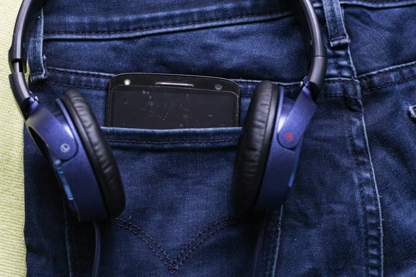 Headphones and a black phone in the back pocket of jeans. Copy S — Stock Photo, Image