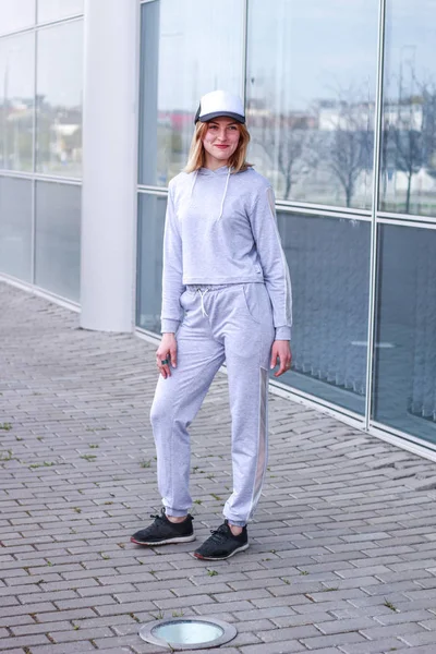 The girl is blonde in a gray sports suit. Street clothing. Sport