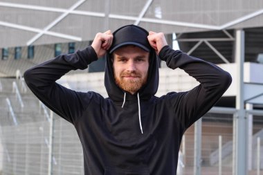 Siyah şapkalı ve siyah kapüşonlu kırmızı sakallı karizmatik adam. 