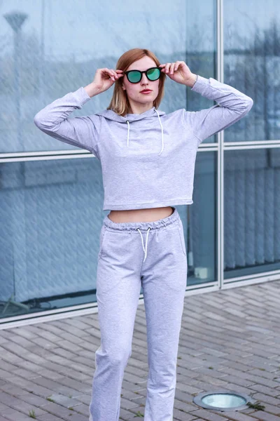 La chica es rubia con un traje deportivo gris. Ropa de calle. Deporte —  Fotos de Stock