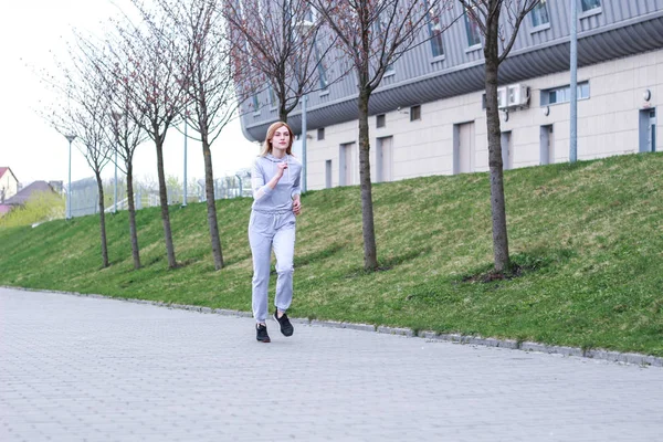 La chica es rubia con un traje deportivo gris. Ropa de calle. Deporte — Foto de Stock