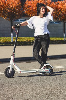 Siyah saçlı kız. Elektrikli scooterla. Sonbahar. Yakınlarda dinlen.