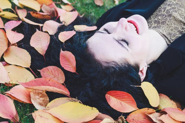 Svarthårig tjej som ligger på gräset med löv i håret. Au — Stockfoto