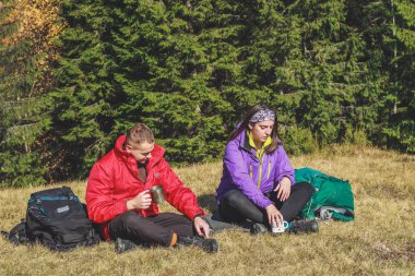 Dağlarda kız ve erkek yürüyüşçüler. Üzerinde çay ve kahve içiyorlar.