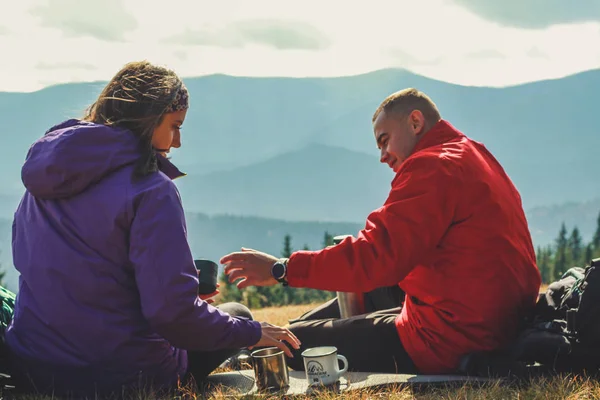 Dağlarda kız ve erkek yürüyüşçüler. Üzerinde çay ve kahve içiyorlar. — Stok fotoğraf