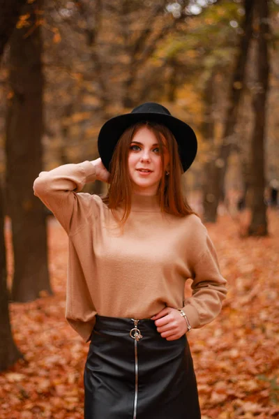 Herfst meisje in het park. Trui, hoed en leren rok. Stijlvol — Stockfoto