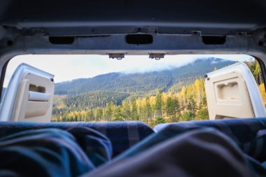 Ukrayna 'da bir kampçıyla seyahat etmek. Sabahleyin karavandan dağlardaki bulutların görüntüsü. Yatak ve bacaklar. Kamp arabasının kapısında biri var..