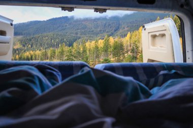 Ukrayna 'da bir kampçıyla seyahat etmek. Sabahleyin karavandan dağlardaki bulutların görüntüsü. Yatak ve bacaklar. Kamp arabasının kapısında biri var..