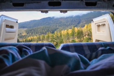 Ukrayna 'da bir kampçıyla seyahat etmek. Sabahleyin karavandan dağlardaki bulutların görüntüsü. Yatak ve bacaklar. Kamp arabasının kapısında biri var..