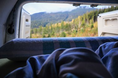 Ukrayna 'da bir kampçıyla seyahat etmek. Sabahleyin karavandan dağlardaki bulutların görüntüsü. Yatak ve bacaklar. Kamp arabasının kapısında biri var..