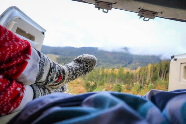 Traveling on a camper in Ukraine. View from the camper in the morning on the mountains in the clouds. Bed and legs. Person in camping van open door.