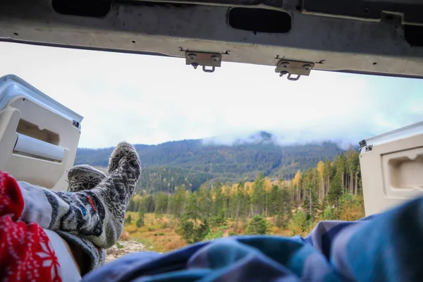 Traveling on a camper in Ukraine. View from the camper in the morning on the mountains in the clouds. Bed and legs. Person in camping van open door.