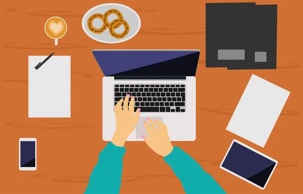 Bir kadın eli bir kahverengi ahşap masa üzerine yerleştirilen bir dizüstü bilgisayar üzerinde çalışıyor. Arka plan olarak orada telefonları, tablet, belge dosyası, kahve fincanı ve çörek.