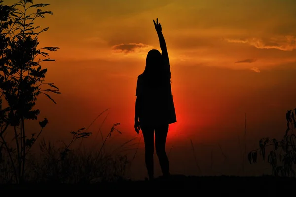 Kollarında ayakta duran bir kadının silueti gün batımı arka planı var