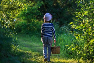 Young girl walking on a path through green woods carrying a basket clipart