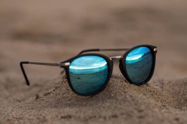 Güneşli yaz sahilde kum ayna yansıması ile yuvarlak güneş gözlüğü.