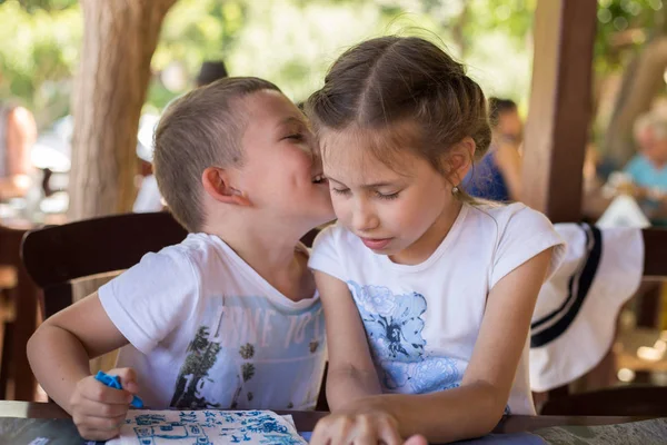 A little boy are whispering something to a pretty girl in a street restaurant. — Stock Photo, Image