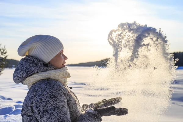 Όμορφη γυναίκα με πλεκτό καπέλο και κασκόλ ρίχνει χιόνι σε ηλιόλουστη χειμωνιάτικη ημέρα — Φωτογραφία Αρχείου