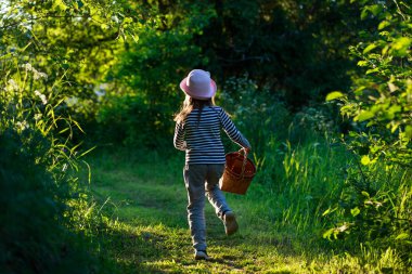 Yeşil ormanda bir sepet taşıyan bir yolda yürüyen genç kız